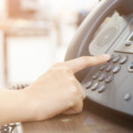 Hand pressing a button on an office telephone.