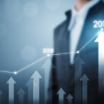 Business professional pointing at a rising graph with upward arrows labeled 2017, 2018, and 2019.