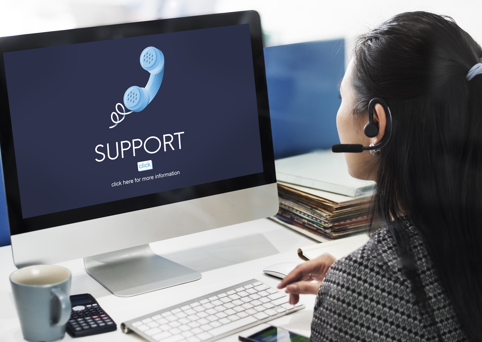 Woman wearing a headset working at a computer with a screen displaying the word "Support" and a phone icon.
