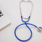 Blue stethoscope placed next to a laptop on a white surface.